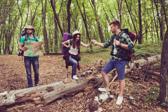 Trust, love, support, help, friendship concept. Three friends are hiking in the spring woods, the guy is holding lady`s hand, bearded man in hat is studying the map