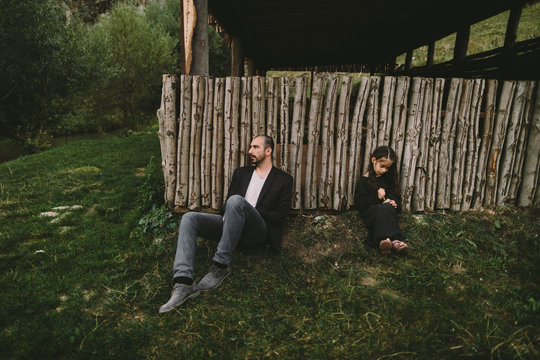 Tired father and daughter sitting at wooden wall