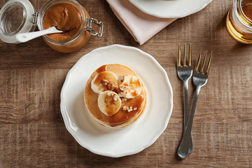 Plate with yummy banana pancakes on wooden table