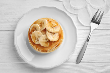 Plate with yummy banana pancakes on wooden table