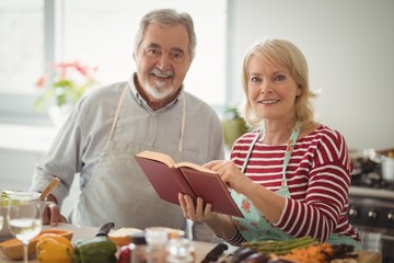 Smiling senior couple with recipe book standing in kitchen