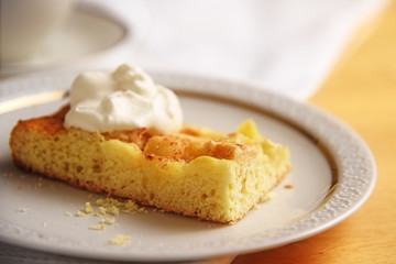 piece of homemade apple cake with whipped cream on a white plate, close up, copy space