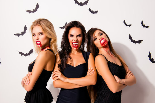 Trick or treat! Terrifyng nightmare. Group of three hot thirsty angry vamps with bloody mouthes, red lips, standing with crossed hands in dark dress, agressive, annoyed and willing t kill