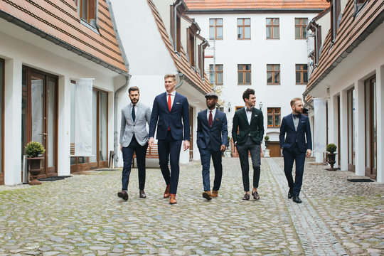 Group of Four Stylish Young Men in Suits Walking Down in Courtyard