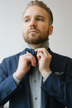 Men's Fashion - Indoor Portrait of Blond Caucasian Man Tying Bow Tie