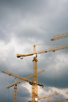 View of construction cranes against stormy clouds