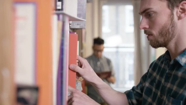 Portrait smiling student standing next to bookcase in shared accommodation.