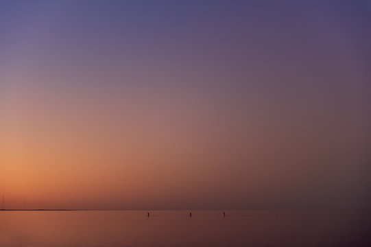 Three stand up paddlers make their way across calm water as the last light of the sun glows beyond the horizon
