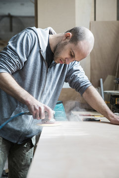 Young carpenter using an electric wood sender in a workshop