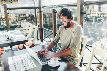 Funny cheerful bearded guy looking at laptop screen and smiling