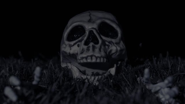Halloween dark night scene with a spooky skeleton skul and arms lying in the grass while thunder and lightning occur at 12, 16, & 27 seconds