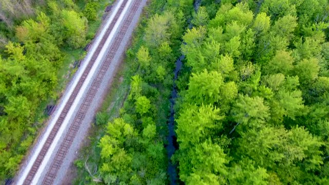 Train tracks run parallel to a small river in an aerial view