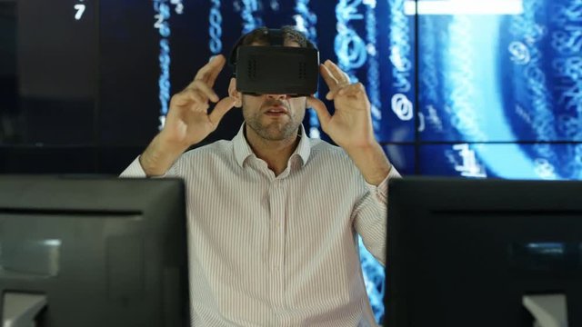  Businessman wearing virtual reality viewer at his desk with animated graphic of digital code in background