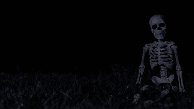 Dark night scene with thunder & lightning occurring at 12, 16, & 27 seconds in behind a grass hill with  a skeleton sitting on the ground.
