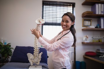 Portrait of smiling female therapist examining artificial spine - Powered by Adobe