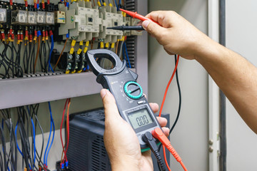 Electrical Engineer adjusts electrical equipment with a multimeter tester in his hand closeup....