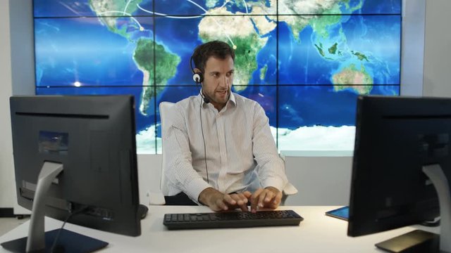  Businessman having conversation via headset with large world map graphic on video wall. Could be global business service agent or airport traffic control room