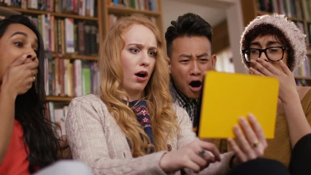 Student friends in shared accommodation reacting to something they see on tablet computer.