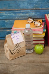Stack of books, apple, water bottle, spectacles and lunch bag