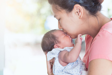 Happy asian mother hugging and kissing her newborn baby with love