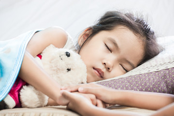 Obraz na płótnie Canvas Cute asian child girl sleeping and hugging her teddy bear with her sister holding hand in the bed