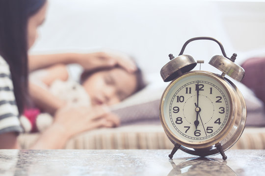 Vintage alarm clock on background of mother taking care asian child girl while she sleeping in the bed