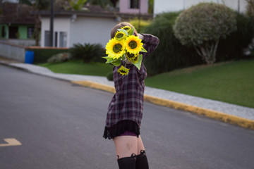 Blodne young woman holding sunflowers by the sunset