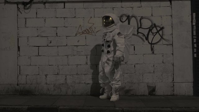  Astronaut in the city at night, standing next to wall with graffiti