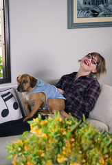 Blonde young woman sitting with her dog on the sofa