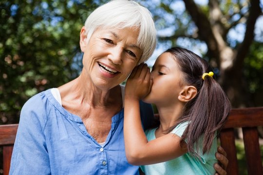 Girl whispering in ears of smiling grandmother