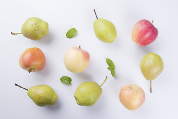 Fresh fruits: apples and pear with mint leaves on a white table.