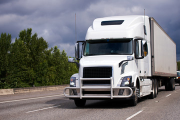 Big rig white semi truck with grille guard and trailer on the road