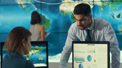  Business team in control room with large world map graphic on video wall - Powered by Adobe