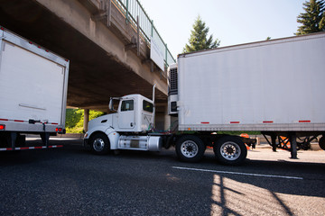 Day cab big rig semi truck going with reefer trailer with refrigeration unit under the bridge on roadside with traffic