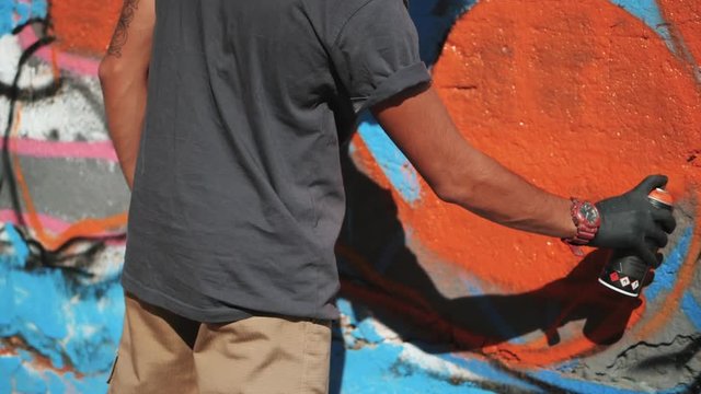 Graffiti Artist Painting On The Street Wall. Male hand with aerosol spray bottle spraying with colorful paint, Urban Outdoors Art Concept. Slow motion.