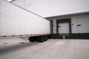 Long dry van semi trailer stand with open door in warehouse dock gate for unload