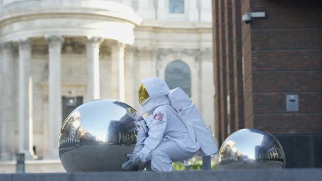  Funny astronaut returned to earth, trying to pick up a metal sphere sculpture