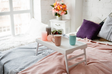 Modern bedroom in pastel colors. Coffee and strawberries on small table decorated candles. Delicious breakfast in bed, romantic concept and tendance between couples