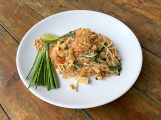 Pad Thai, stir-fried rice noodles with shrimp in white plate on wood table. The one of Thailand's national main dish. the popular food in Thailand. Thai Fried Noodles