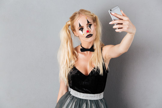 Pretty blonde woman in halloween clown make-up taking a selfie