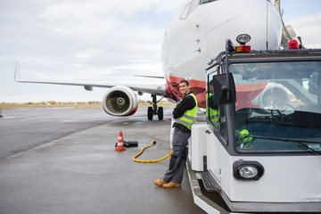 Fototapeta na wymiar Worker Leaning On Towing Truck With Airplane In Background