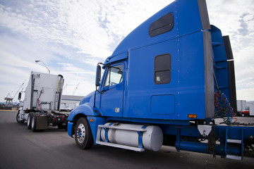 Two big rigs semi trucks tractors standing on the parking lot in industrial area