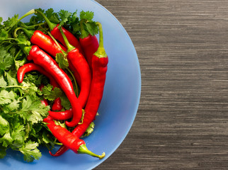 Red cayenne peppers (Capsicum annuum) and verdure in blue bowl on wooden table. Top view. Aso known as Guinea spice, cow-horn pepper, red hot chili pepper, aleva, bird pepper.