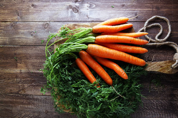 Fresh organic carrots with green leaves on wooden background. Ve