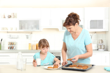 Cute little girl and her grandmother tasting cookies on kitchen