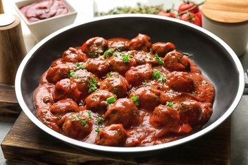 Frying pan with delicious meatballs in tomato sauce on table