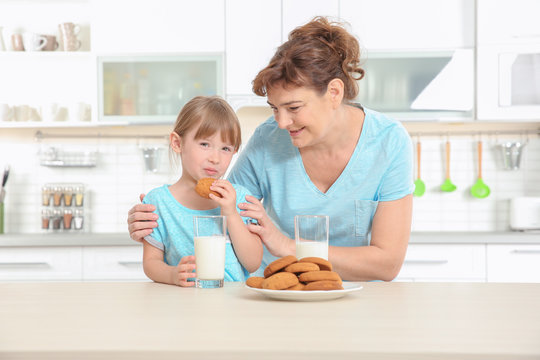 Cute little girl and her grandmother tasting cookies on kitchen