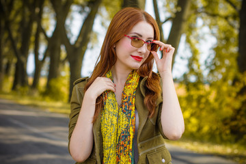 Fototapeta premium A young woman is stylishly dressed in green and red shades standing in an autumnal grove of trees in vintage glasses