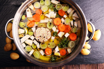 Broth with carrots, onions various fresh vegetables in a pot - colorful fresh clear spring soup. Rural kitchen scenery vegetarian bouillon or stock