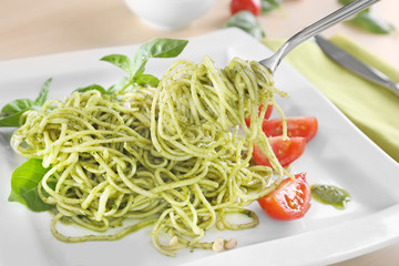 Delicious pasta on fork with pesto sauce over plate, closeup
